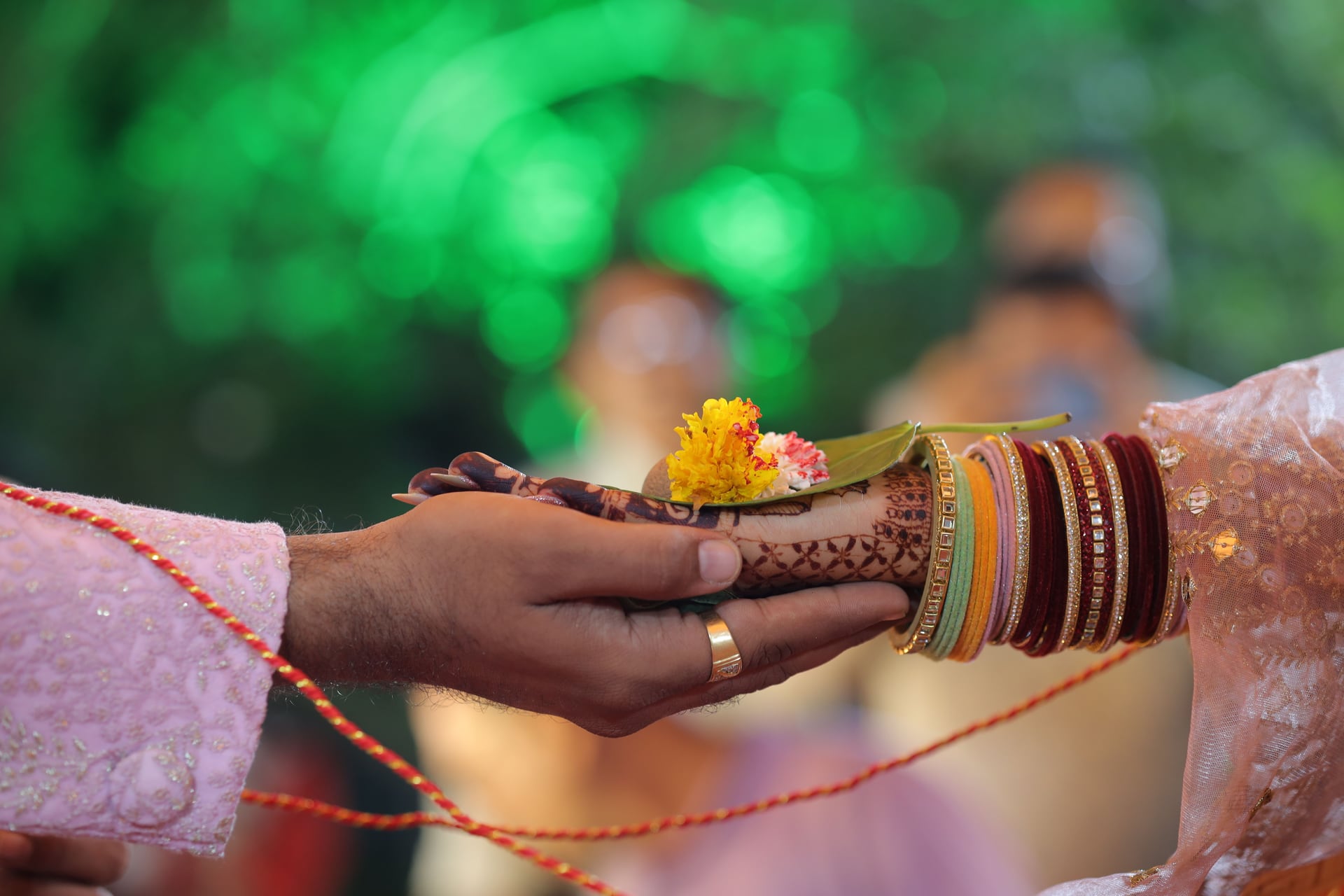 Wedding ceremony hands with mehendi, bangles and flowers
